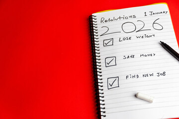 2026 goals list with push pins, an indoor plant and a sticky note on red background. Creative New...