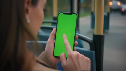 Close-up of a woman commuting on a bus, swiping on a smartphone with a vertical green screen display for mockup. - Powered by Adobe