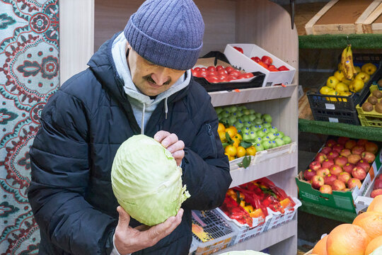 Mature man carefully inspecting head of fresh green cabbage at market stall