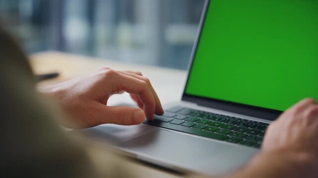 Cinematic close-up of male hands typing on keyboard, green screen laptop display.