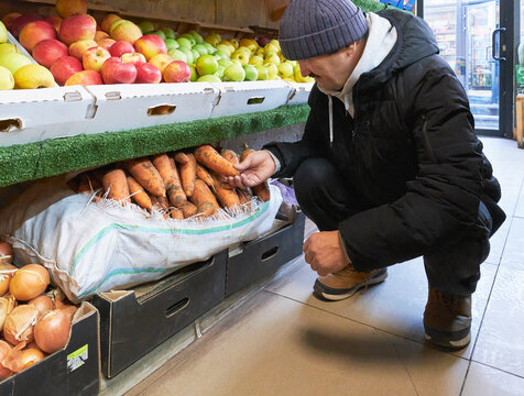 Senior man squatting to select fresh carrots from sack at grocery market