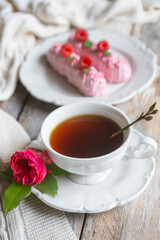 A cup of aromatic, hot tea and raspberry eclairs on a light table.