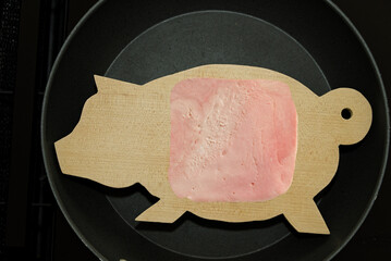 Schinken auf Holzteller in Schweineform in der Pfanne