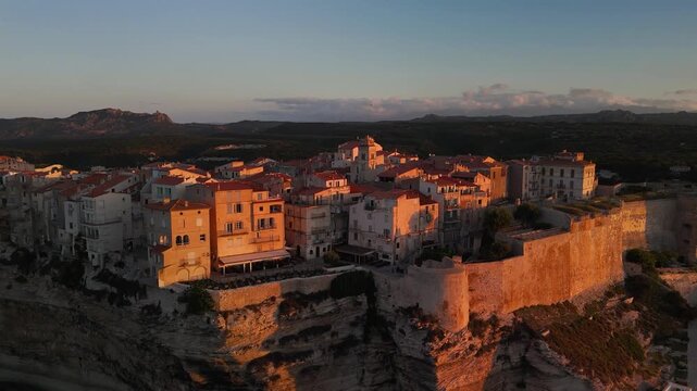 Expansive Aerial Drone Approach Shot Gliding Over the Mediterranean Sea Towards the Historic Bonifacio Citadel City Perched on Dramatic White Limestone Cliffs at Golden Hour Sunrise, Corsica, France.