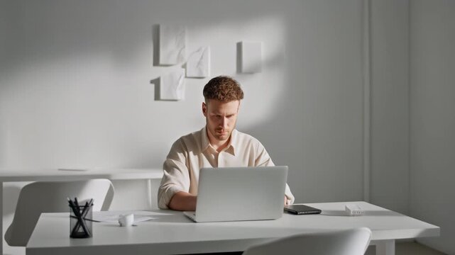 Man working on a laptop in a minimalist office with white walls and bright natural light