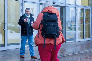 Obraz premium Female photographer in red jacket filming man with phone and coffee cup in snowy weather outside modern business center. High quality photo