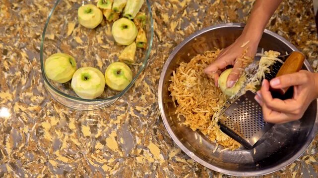 Closeup view of grating fresh apples on a hand grater. Simple food preparation process in a home kitchen environment.