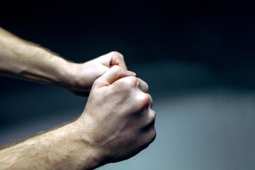 Close-up of clenched male hands expressing tension, stress, and emotional pressure against a dark...