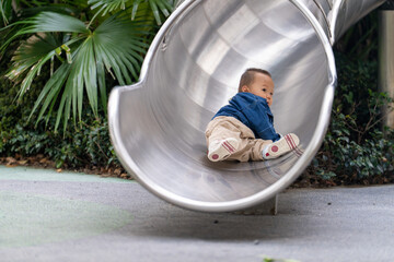 A 16-month-old Asian baby boy in denim shirt playing on a slide outdoors