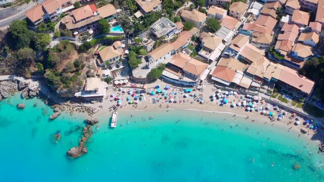 People in Greece on a beach in bay with small village and restaurants. Agios Nikitas vacation on greek island. Aerial overhead top down shot
