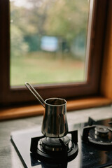 Coffee kettle sits on a small gas stove in a cozy kitchen by a window, warm light filters through, a calm brewing moment captured in the intimate home scene