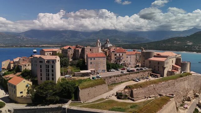 Expansive Aerial Drone Pan Out Shot Revealing the Medieval Calvi Citadel Fortress, Harbor, and Historic Town on the Mediterranean Coastline of Corsica, France.