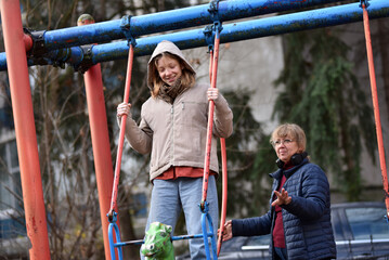 Obraz premium Mother and teenager daughter playing on a swing set outdoors in an urban park