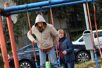 Mother and teenager daughter playing on a swing set outdoors in an urban park