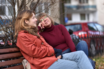 Fototapeta premium Teenager daughter and mother resting on a park bench in autumn