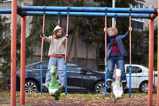 Mother and teenager daughter playing on a swing set outdoors in an urban park - Powered by Adobe