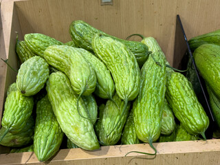 Close-up View of Fresh Green Bitter Melons Piled in a Wooden Crate at a Vibrant Market Stall