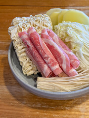 Assortment of Fresh Hot Pot Ingredients with Thinly Sliced Beef, Noodles, Cabbage, and Mushrooms Artfully Arranged on a Ceramic Plate, Ready for Cooking