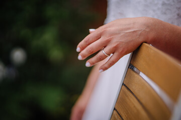 Elegant hand of a woman with a silver ring resting on a wooden chair, surrounded by lush greenery, showcasing a serene and intimate moment in nature