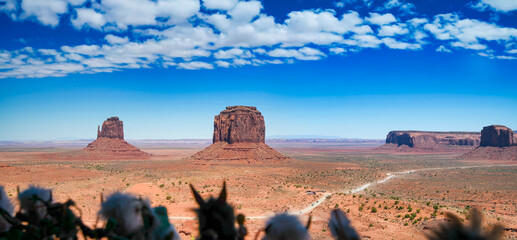 Panoramic view of Monument Valley desert landscape under bright summer sun and clear blue sky