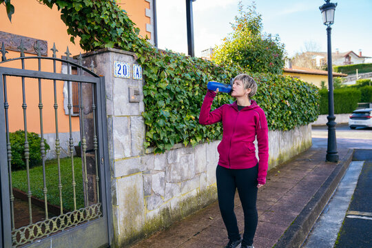 Woman hydrating with a water bottle during a workout on a quiet street, promoting healthy lifestyle and fitness