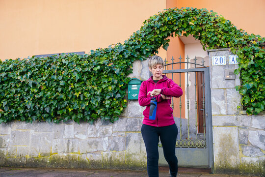 Woman adjusting her fitness tracker, holding a water bottle, preparing for a healthy outdoor workout or running session