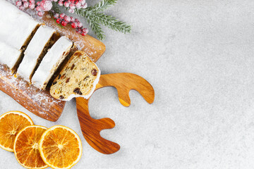 Traditional Christmas stollen, sweet fruit loaf sliced on wooden board, dusted with powdered sugar on white textured background, copy space. Spices, dried fruits and festive decor, winter holiday mood