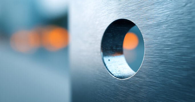 Close-up of a brushed metal surface with a circular hole and blurred orange lights in the background creating an abstract industrial composition