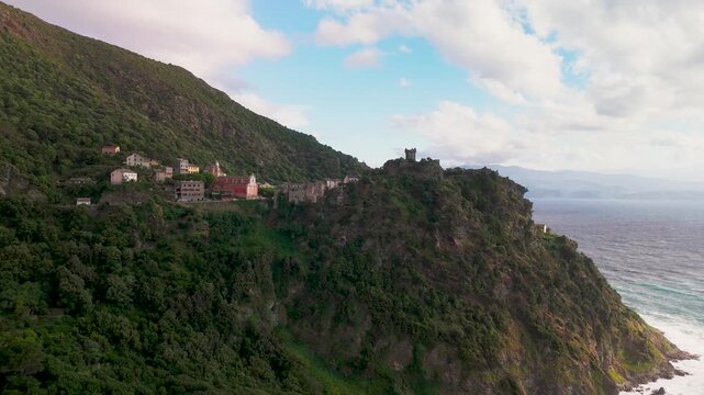 Cinematic Aerial Pan Across Nonza Village, Highlighting Historic Paoline Tower Ruins and Colorful Houses Perched on a Dramatic Steep Cliff Above the Mediterranean Sea, Cap Corse, Corsica, France.
