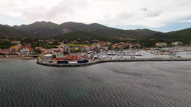 Smooth Cinematic Aerial Approach Shot Flying Over Clear Mediterranean Sea Towards Macinaggio Village and Harbor in Cap Corse, Corsica, France.