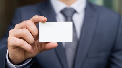 Fototapeta premium A man in a suit holding a blank white card in his hand in front of his chest and tie area