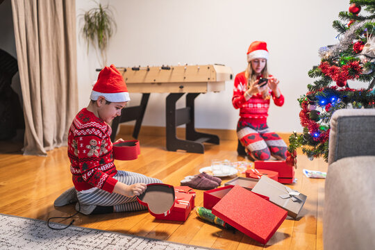 Children expressing joy and excitement while opening presents on christmas morning, wearing festive sweaters and santa hats by a decorated tree