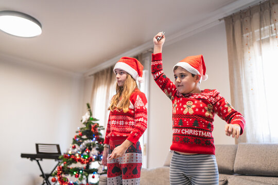 Siblings in holiday sweaters playing a video game at home during christmas, enjoying festive family time and fun