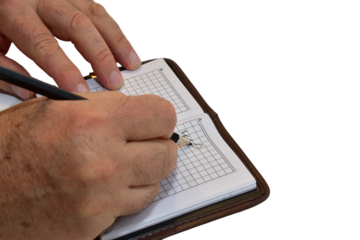 A man scribbles something on the pages of a notebook with a pencil.