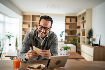 Obraz premium Smiling man breakfasting at home while engaging in video call