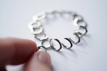 Hand Connecting Silver Chain Links Together on White Background, Illustrating Connection, Unity, Relationship, and Dependence