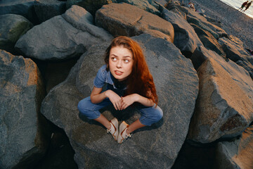 Lifestyle woman in modern boho-western denim street style sitting on rocks with film color effect, capturing relaxed and natural outdoor vibe near water.