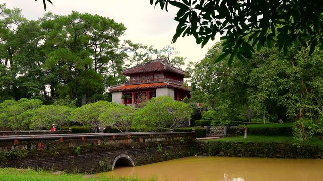 Minh Lau Pavilion viewed across a stone bridge, surrounded by lush gardens and pines at Minh Mang Tomb.