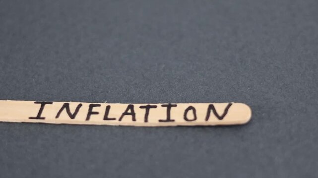 Un primer plano de una paleta de madera con la palabra de inflaci&oacute;n y en un fondo gris oscuro. Pol&iacute;tica econ&oacute;mica 