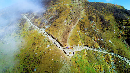 Aerial drone shot people devotees climbing narrow stair covered path of Tungnath Trek from Chopta to get to world's highest Shiv temple on barren stony mountains covered in clouds Uttarakhand India