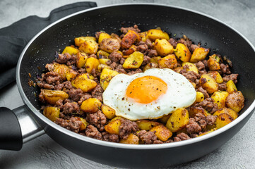 Beef hash with fried potatoes, ground beef and sunny egg in skillet on gray surface with dark napkin, perfect for rustic cooking themes.