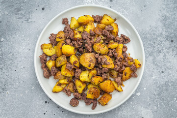 Crispy fried potatoes with ground beef served on a white plate, hearty homemade hash on a rustic grey background.