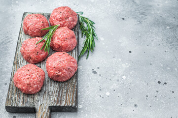 Uncooked meatballs or cutlets with herbs and seasoning on weathered board highlighting raw texture for culinary and butcher visuals.