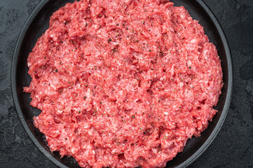 Fresh raw ground mince beef and pork meat with seasoning on black plate over dark textured background ideal for cooking, butcher and protein ingredient themes.