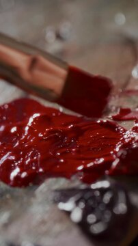 Extreme close-up view of brush blending vibrant red and dark burgundy paints on artistic palette during color preparation