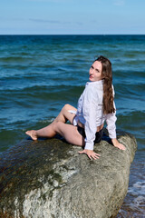 Young woman portrait sitting on rock by Baltic Sea under clear sky