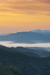 Misty mountain landscape with layered hills under warm orange sky at sunrise, creating peaceful and serene atmosphere