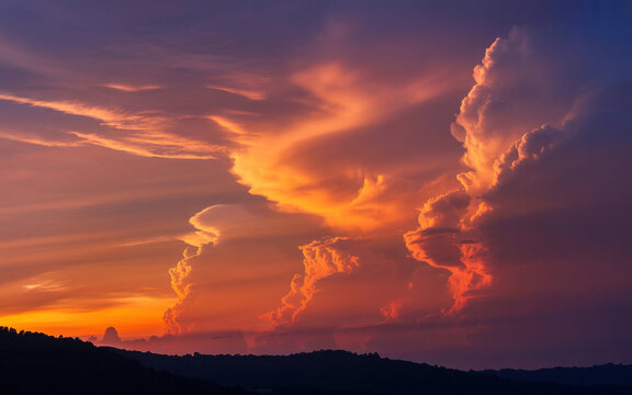 Dramatic sunset clouds painted with vibrant orange and purple hues over rolling hills