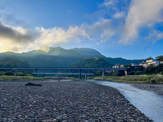 Scenic autumn morning at Wulai river valley, New Taipei City, Taiwan. Mountain landscape with bridge, flowing stream, pebble riverbed and misty clouds.