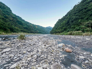 Morning view of Wulai river gorge in New Taipei City, Taiwan. Clear stream flows through rocky riverbed surrounded by lush green mountain slopes.